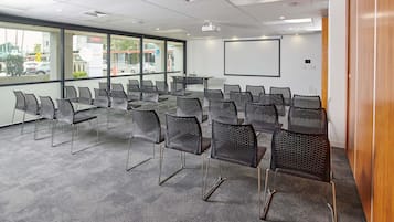 Ein Konferenzraum mit Reihen von Stühlen, einer Projektionsleinwand und großen Fenstern.