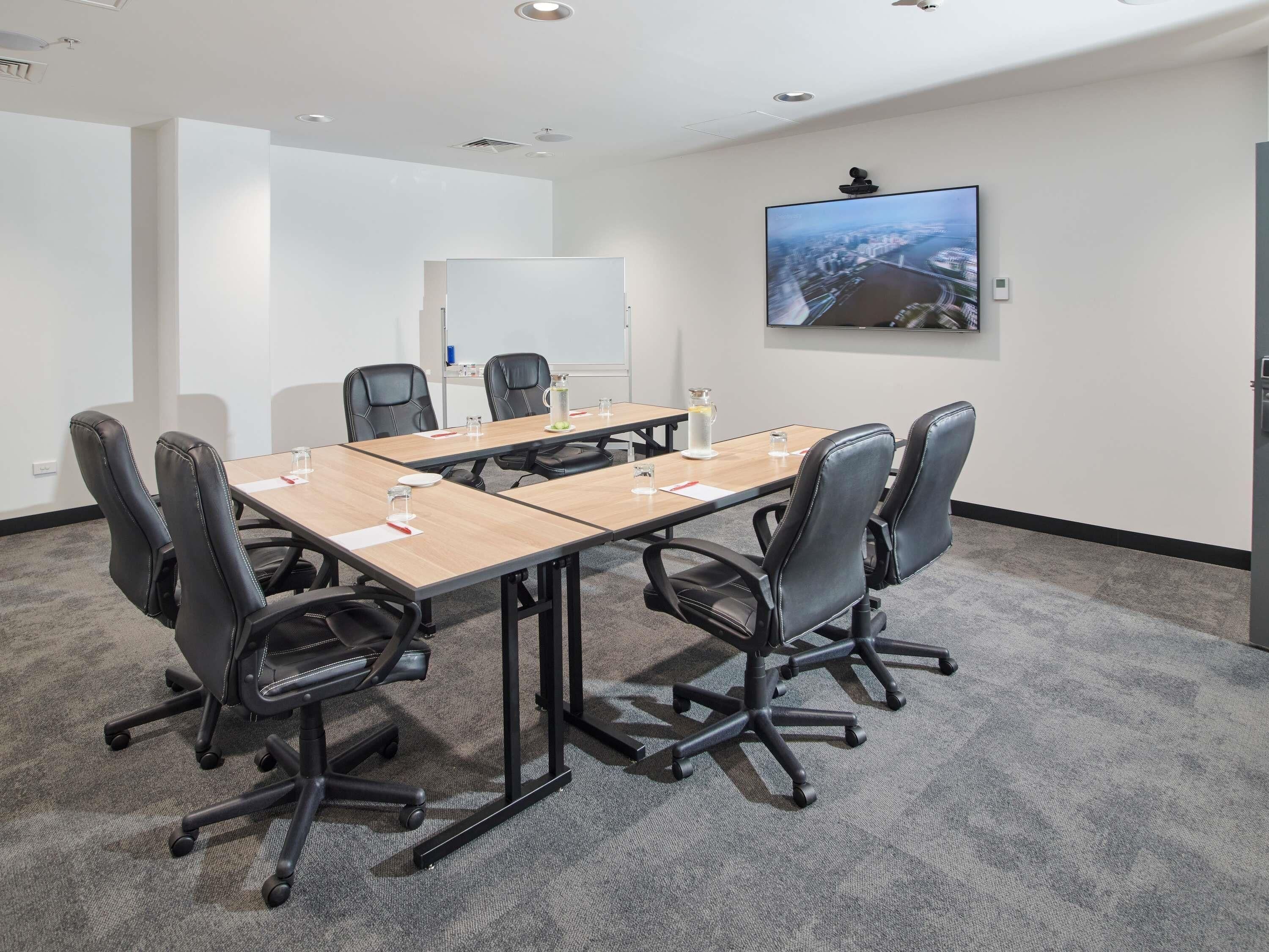 Une salle de conférence avec une longue table, six chaises, un tableau blanc et une grande fenêtre donnant sur le paysage urbain.