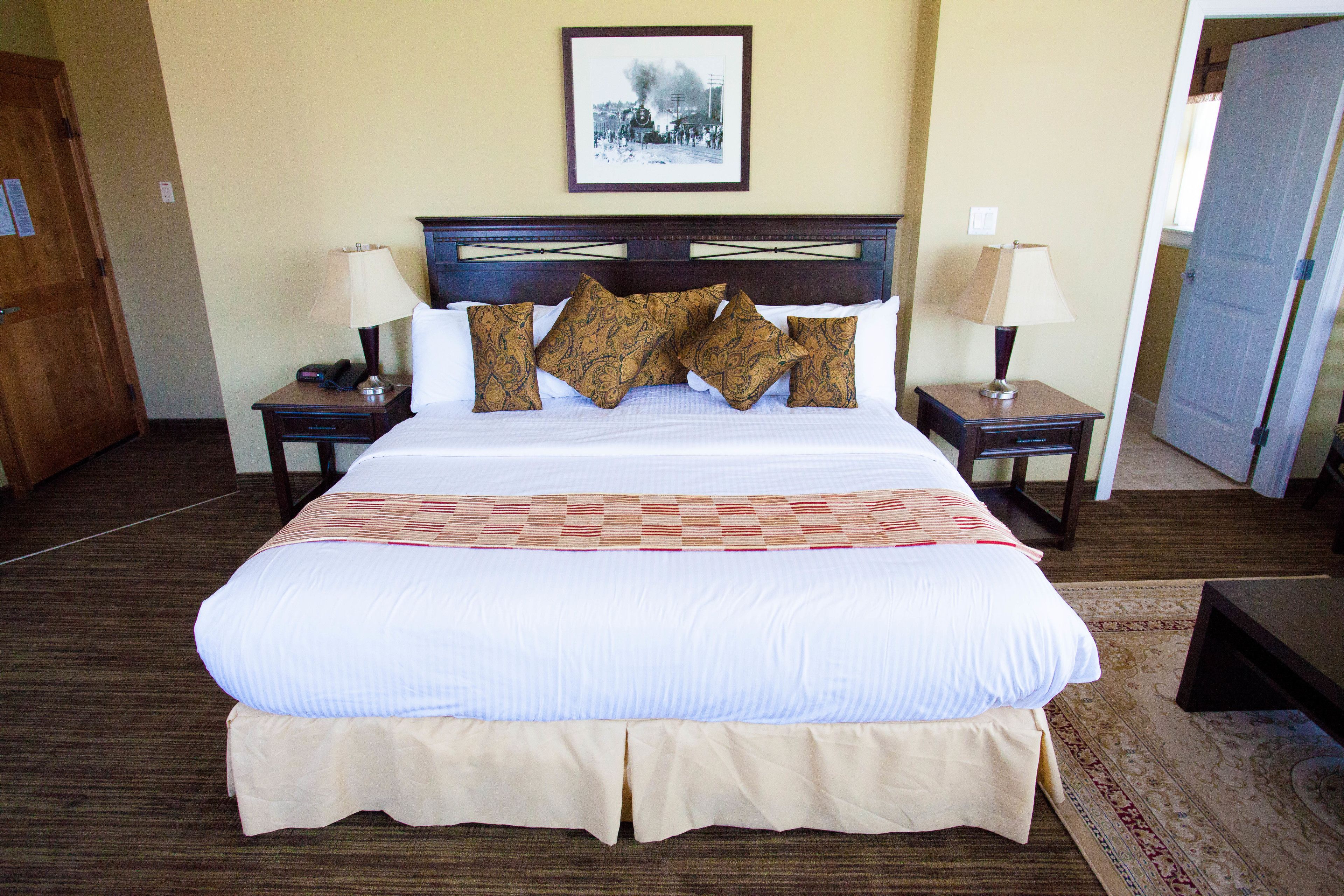 A neatly made bed with patterned pillows, two bedside tables with lamps, a framed picture on the wall, and a wooden door.