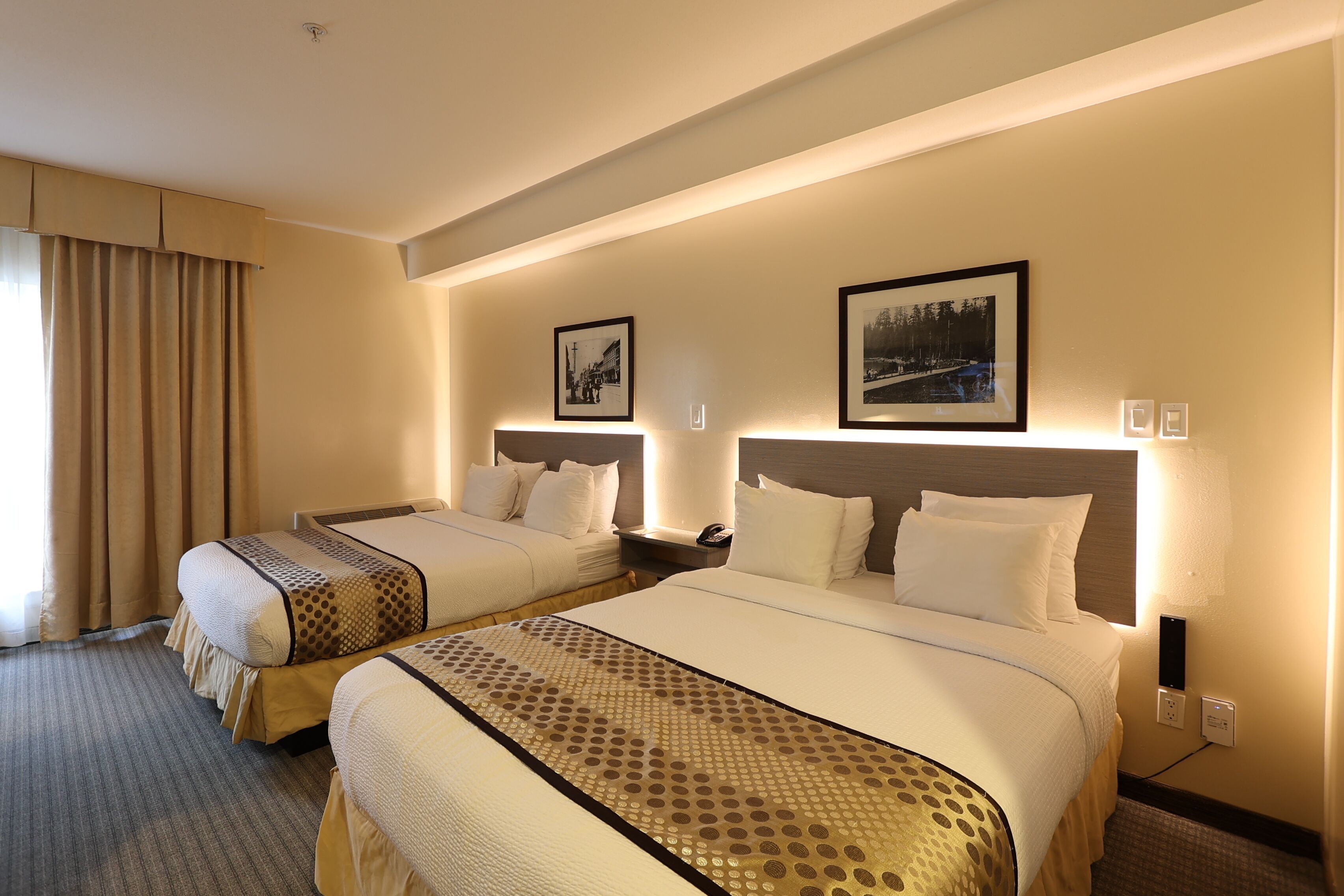 A hotel room with two beds, a large window with curtains, and two framed pictures on the wall.