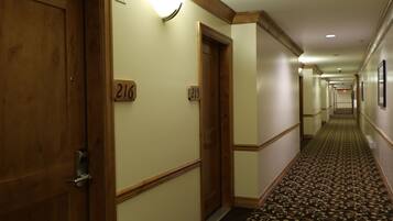 Pasillo de hotel con puertas de madera, placas de número de habitación y una alfombra estampada.
