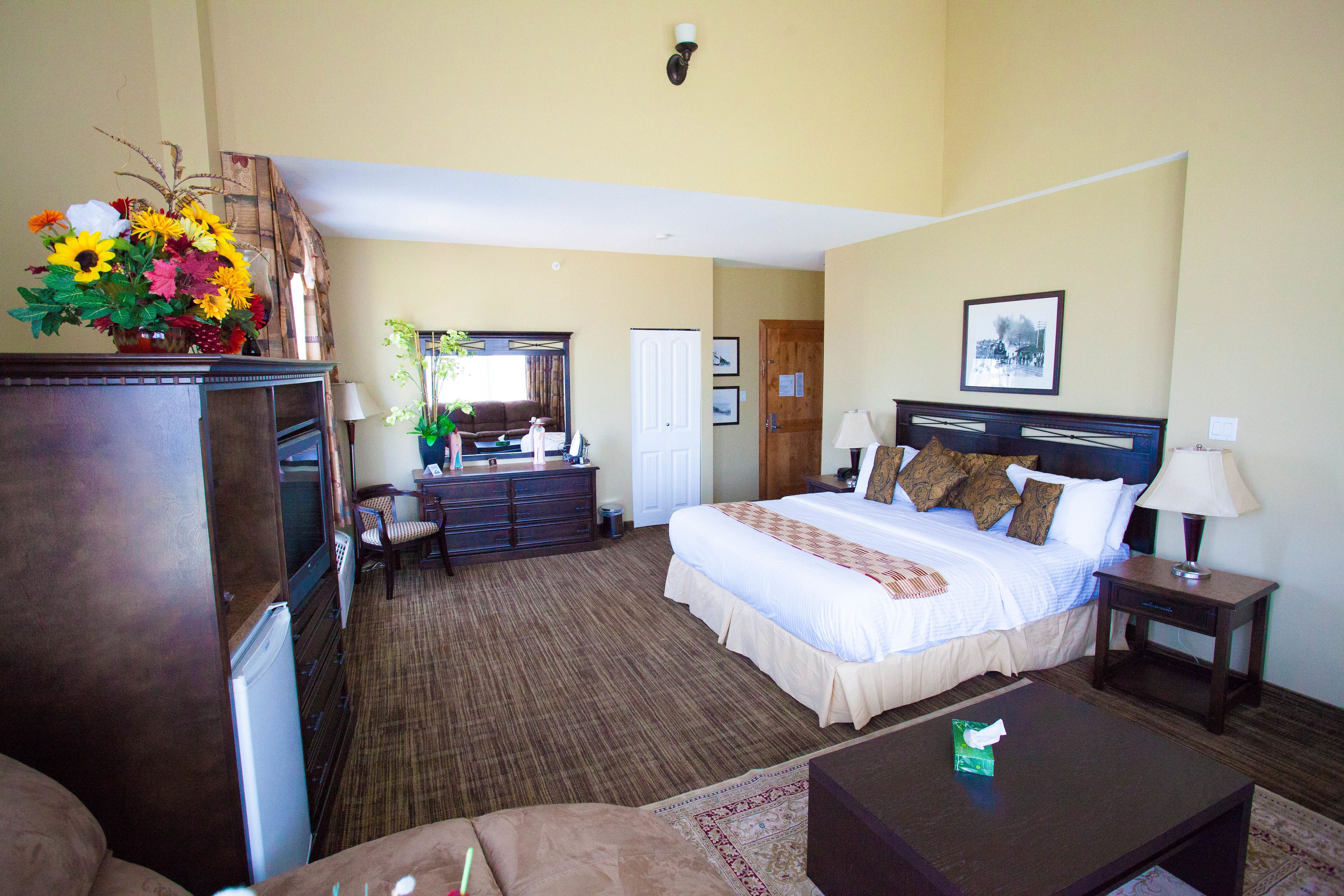 A hotel room with a bed, a desk, a dresser, a television, and a flower arrangement.