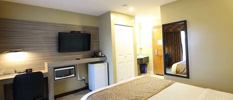 A hotel room with a bed, desk, microwave, and television.