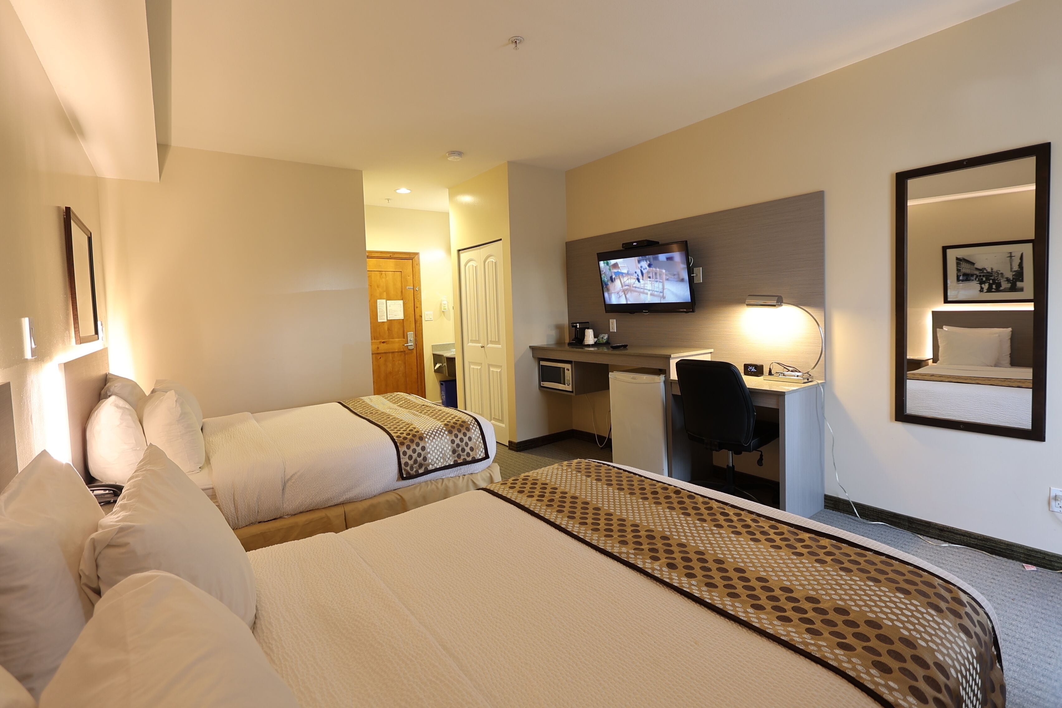 Une chambre d’hôtel avec deux lits, un bureau, une télévision et un miroir.