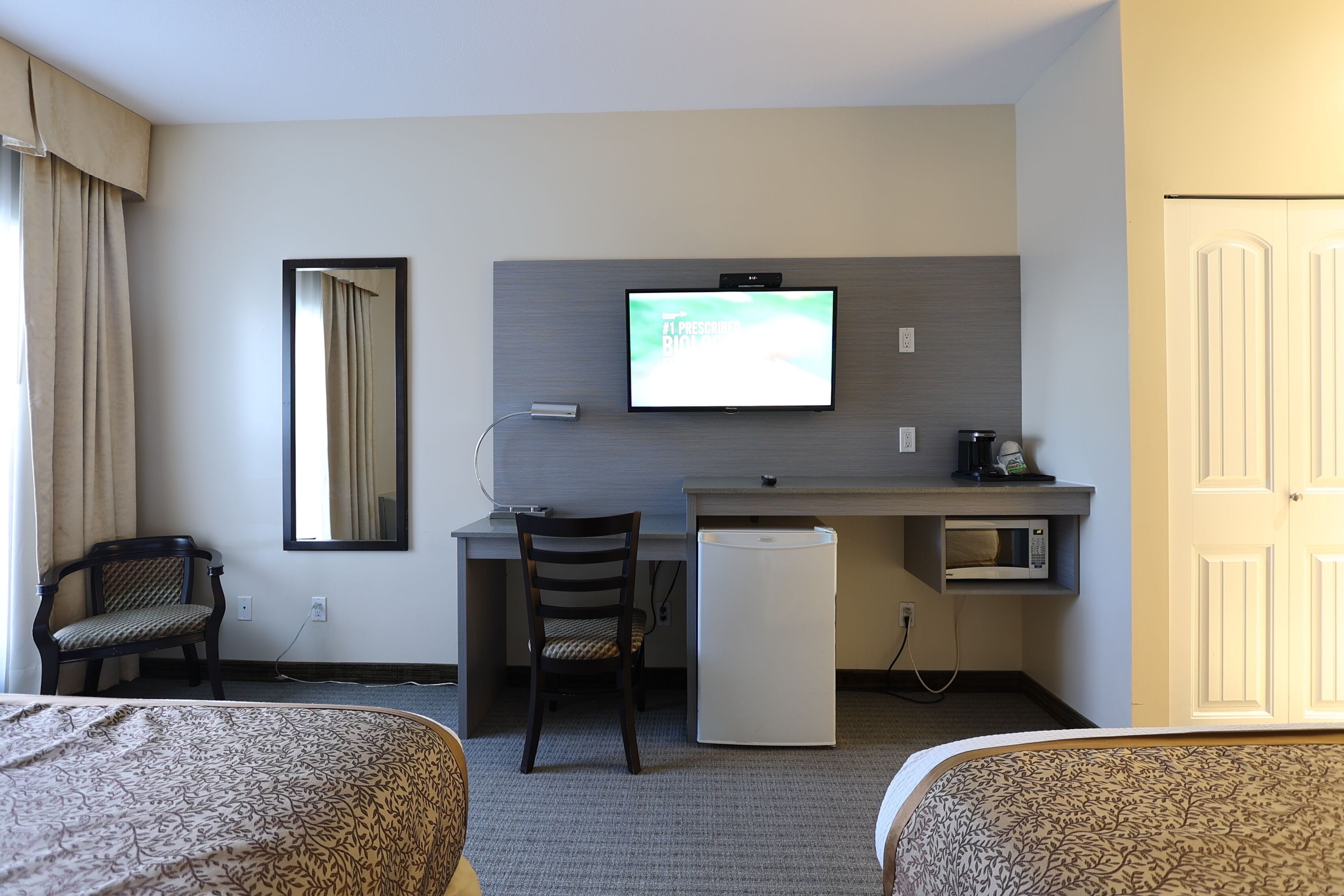 Une chambre d’hôtel avec deux lits, un bureau avec un ordinateur, une chaise, un four à micro-ondes et un téléviseur.