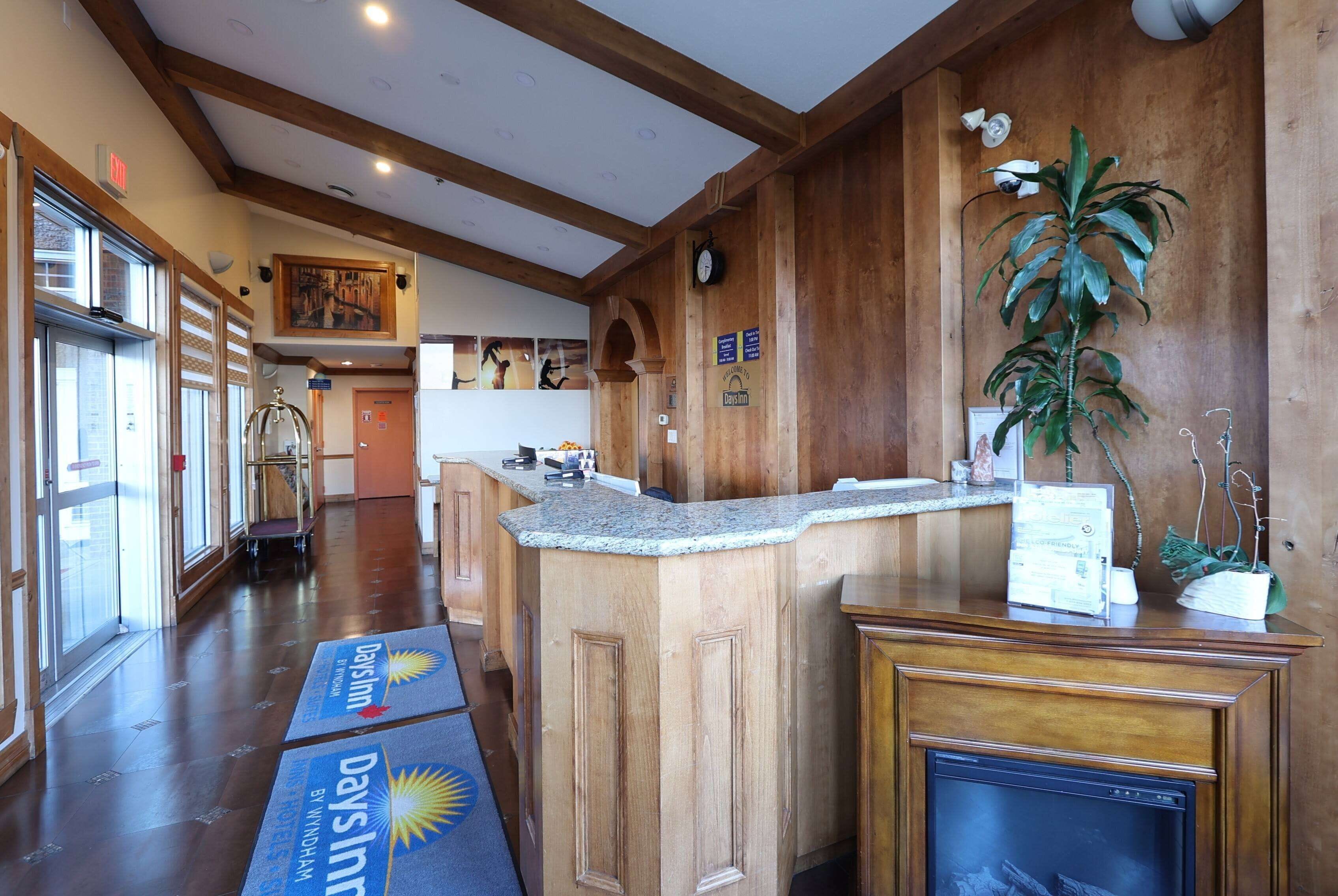 A hotel lobby with wooden paneling, a reception desk, a fireplace, and a large plant.