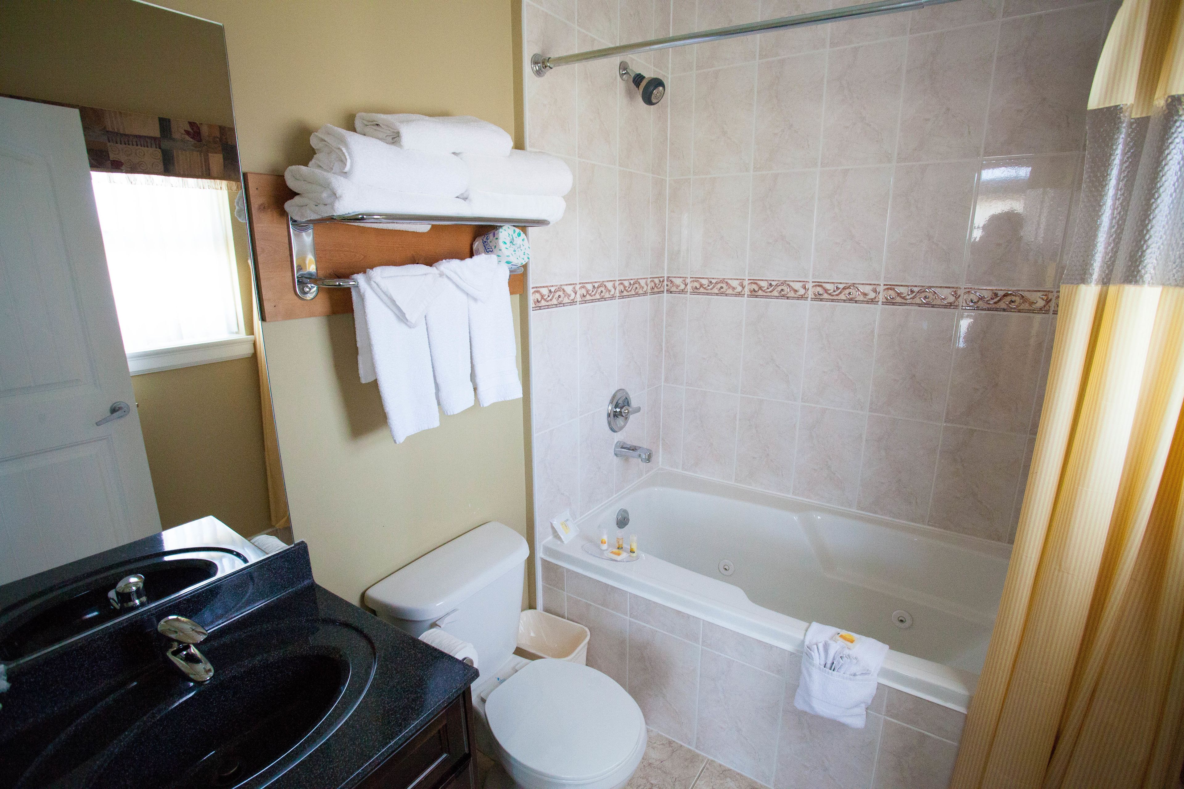 A bathroom with a black sink, white toilet, and a bathtub. There are towels on a rack and a shower curtain.