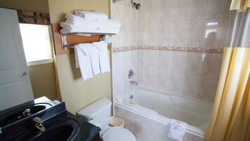 A bathroom with a black sink, white toilet, and a bathtub. There are towels on a rack and a shower curtain.