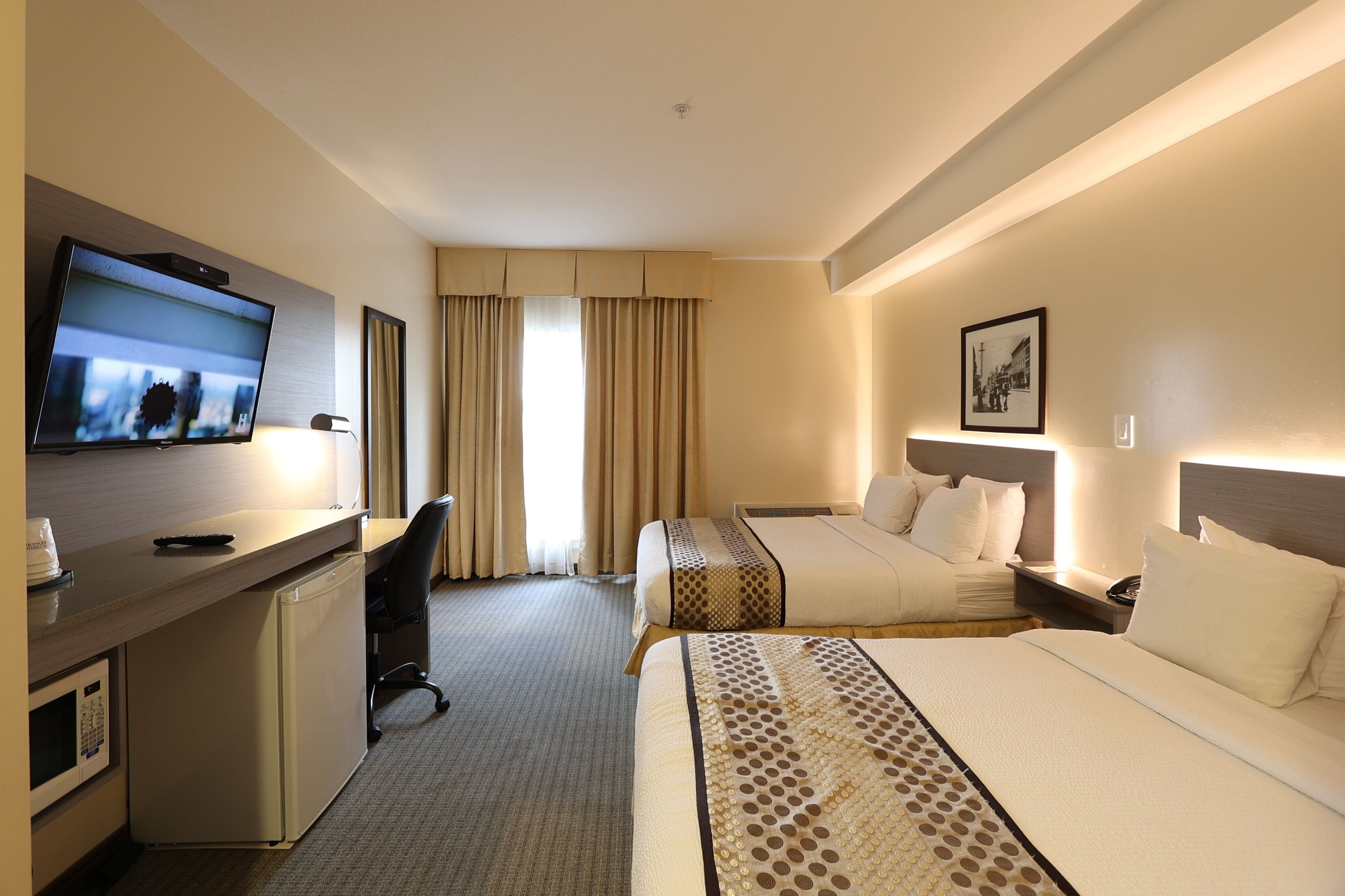 Habitación de hotel con televisión, escritorio, dos camas, microondas y ventana con cortinas.