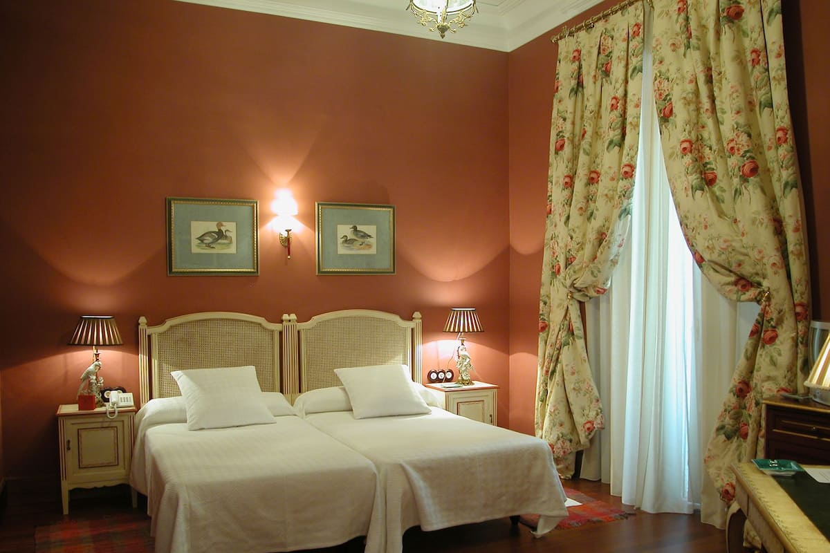 A double bed with two nightstands, a wall-mounted lamp, and a floral curtain.