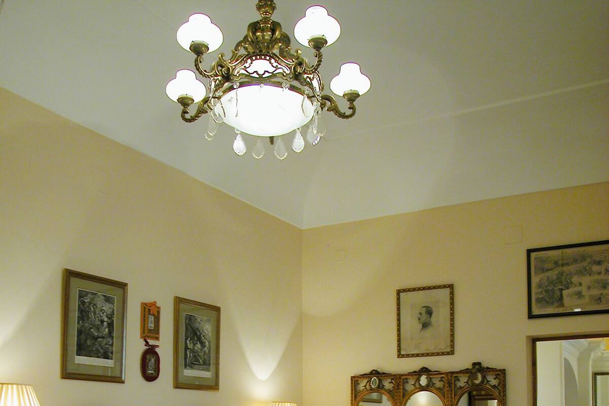 A bedroom with a large bed, two bedside tables with lamps, a wooden dresser, and a chandelier.