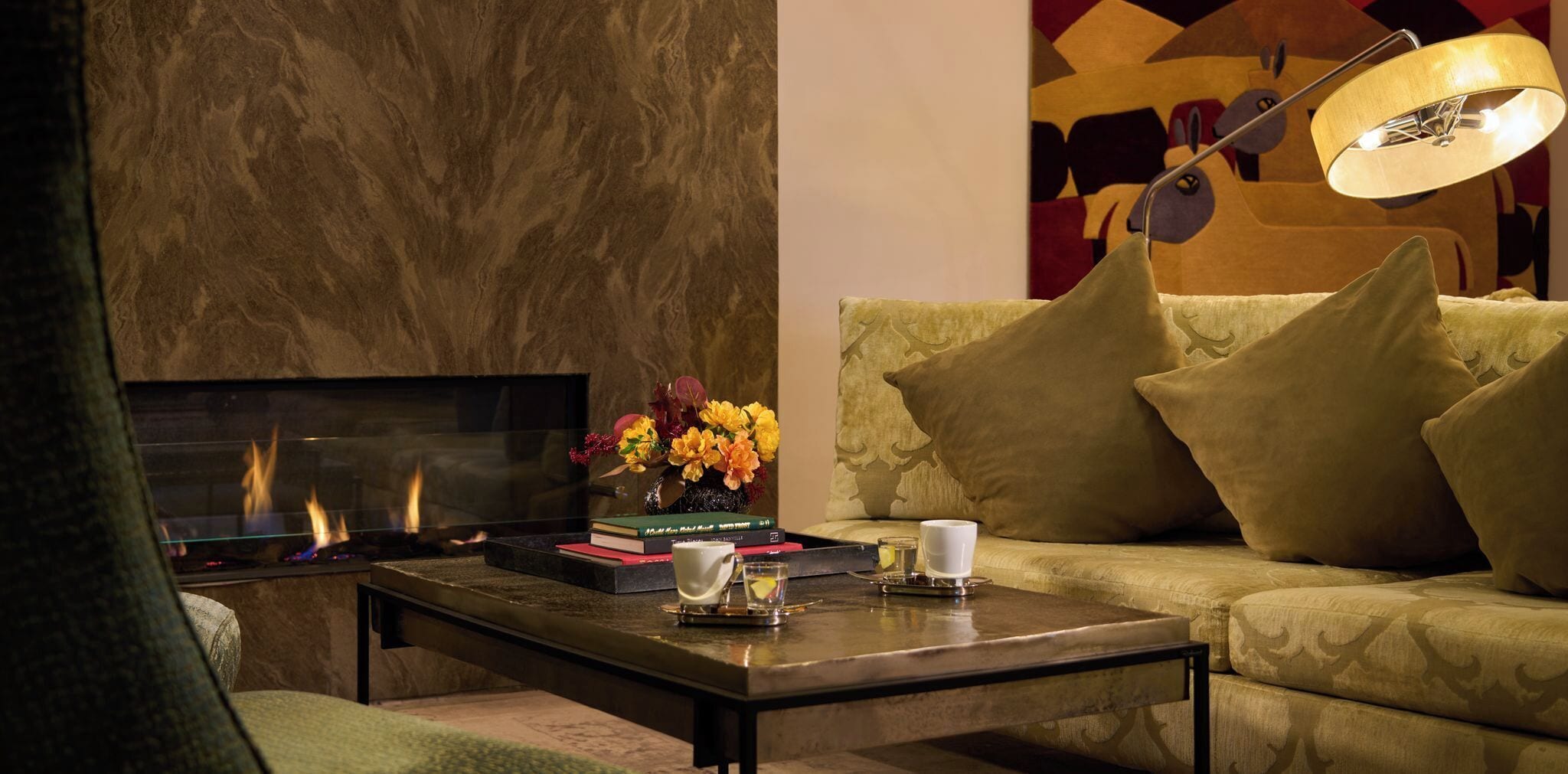A living room with a fireplace, a sofa, a coffee table with books and a vase of flowers, and a lamp.