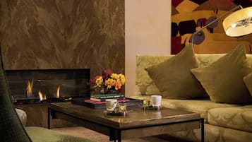 Una sala de estar con chimenea, un sofá, una mesa de centro con libros y un jarrón de flores, y una lámpara.