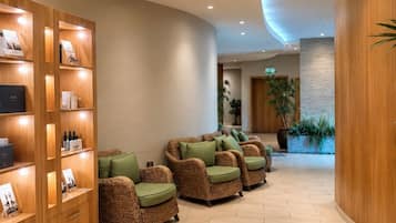 A reception area with a curved ceiling, wooden reception desk, wicker chairs with green cushions, and a potted plant.