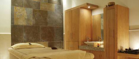 A bathroom with a stone wall, wooden cabinets, a bed, and a sink.