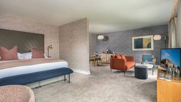 A modern hotel room with a large bed, a seating area with a sofa and armchair, a dining table, and a TV.