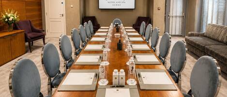 A conference room with a long table, chairs, and a projector screen displaying hotel information.
