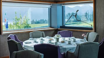 Ein Essbereich mit einem Tisch für vier Personen, Stühlen, einem Fenster mit Blick auf Grünflächen und Berge sowie einem dekorativen Insekt auf der Fensterbank.