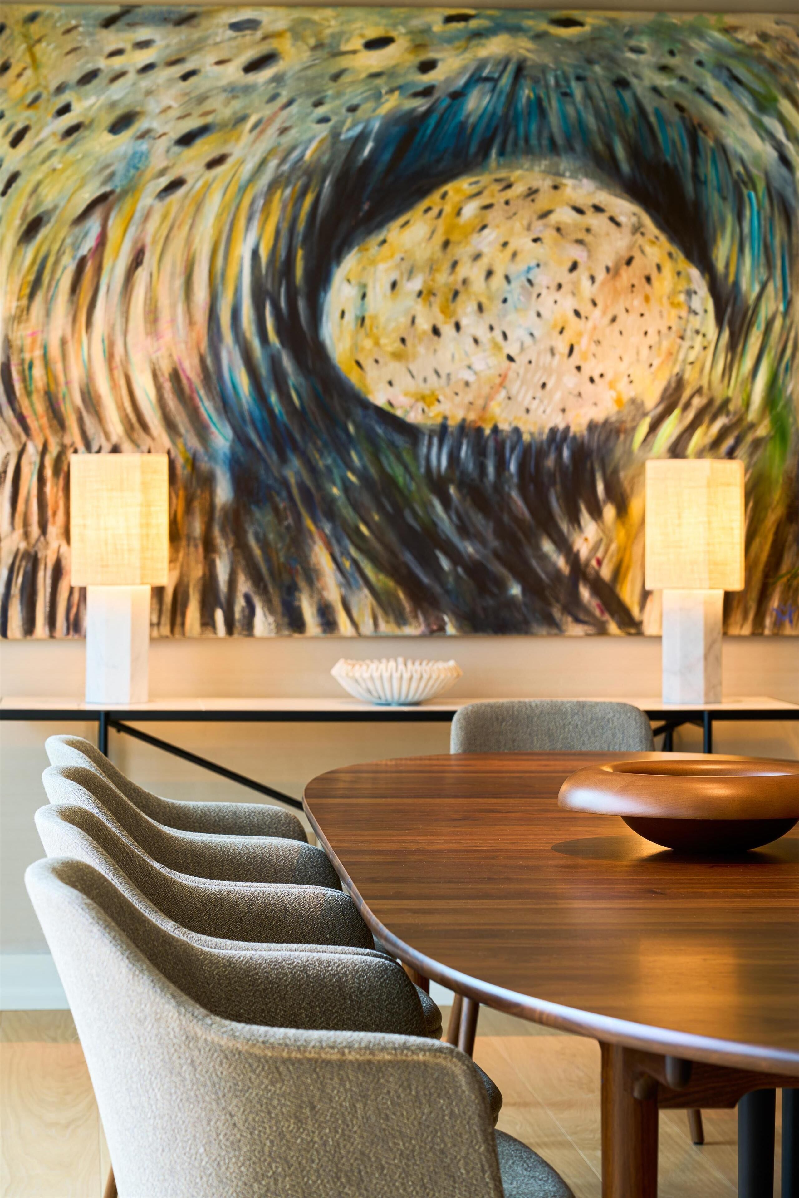 A dining area with a wooden table, grey upholstered chairs, and a large abstract painting on the wall.