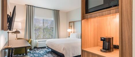 A hotel room with a bed, a desk with a lamp, a coffee maker, a microwave, and a window with curtains.