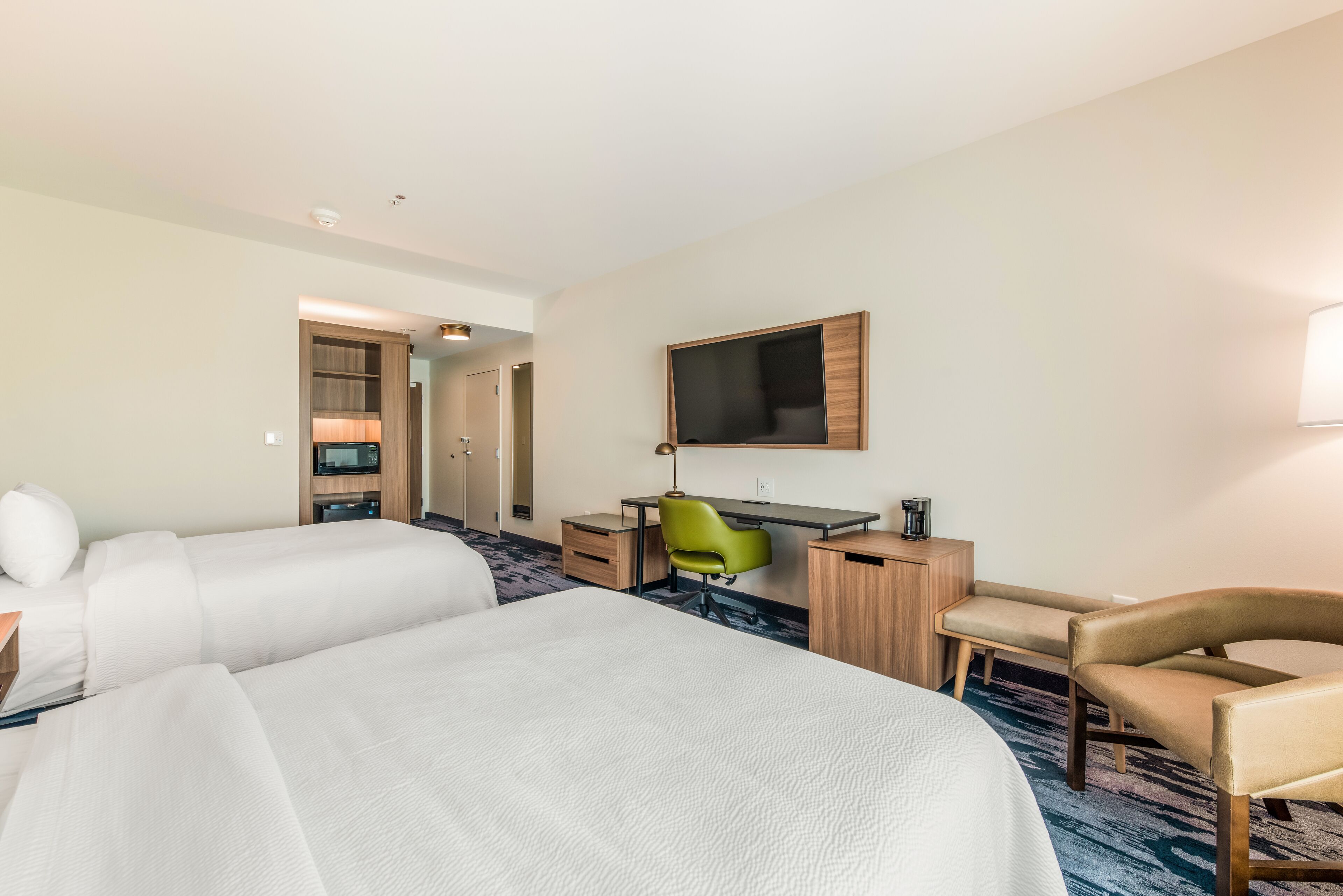 A hotel room with two beds, a desk, a chair, a TV, and a wardrobe.