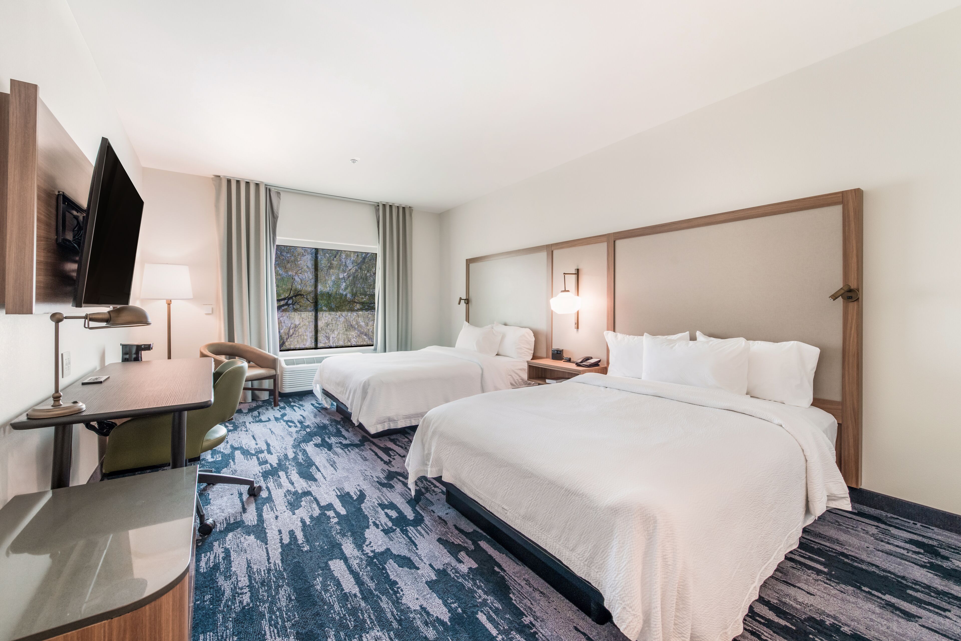 A hotel room with two beds, a desk, a TV, and a window with curtains.