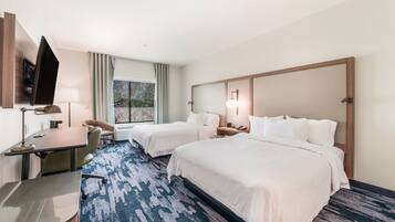 A hotel room with two beds, a desk, a TV, and a window with curtains.