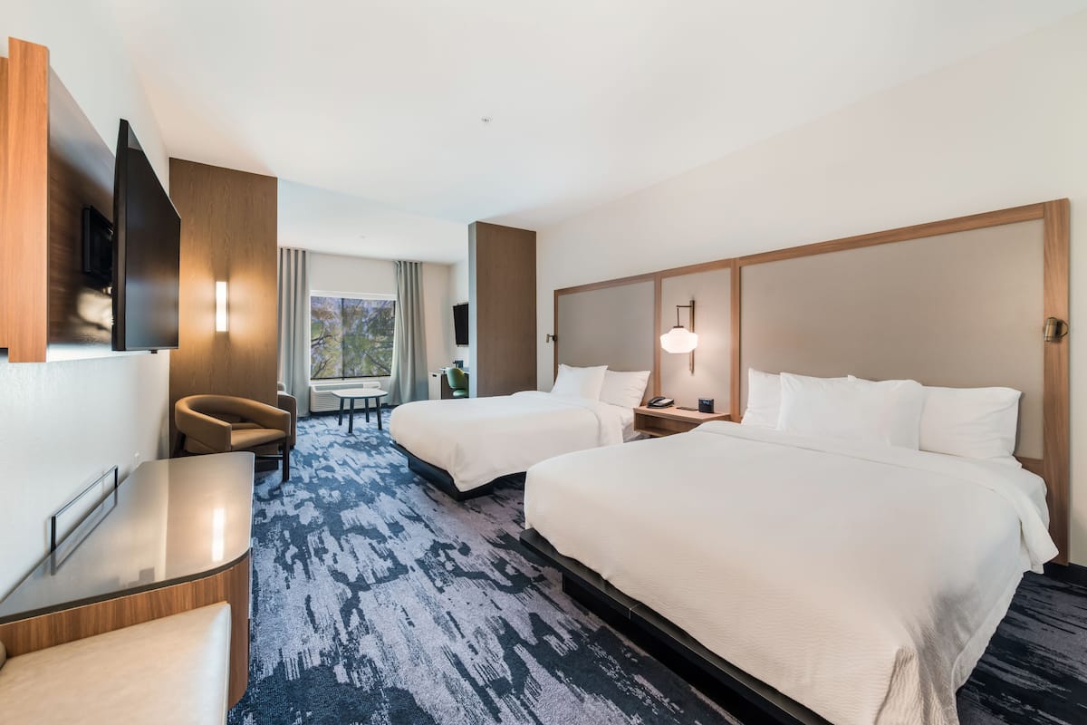 A hotel room with two beds, a desk, a chair, a TV, and a window with curtains.