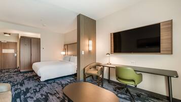 A hotel room with a bed, desk, chair, and a TV mounted on the wall.