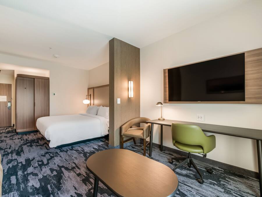 A hotel room with a bed, desk, chair, and a TV mounted on the wall.