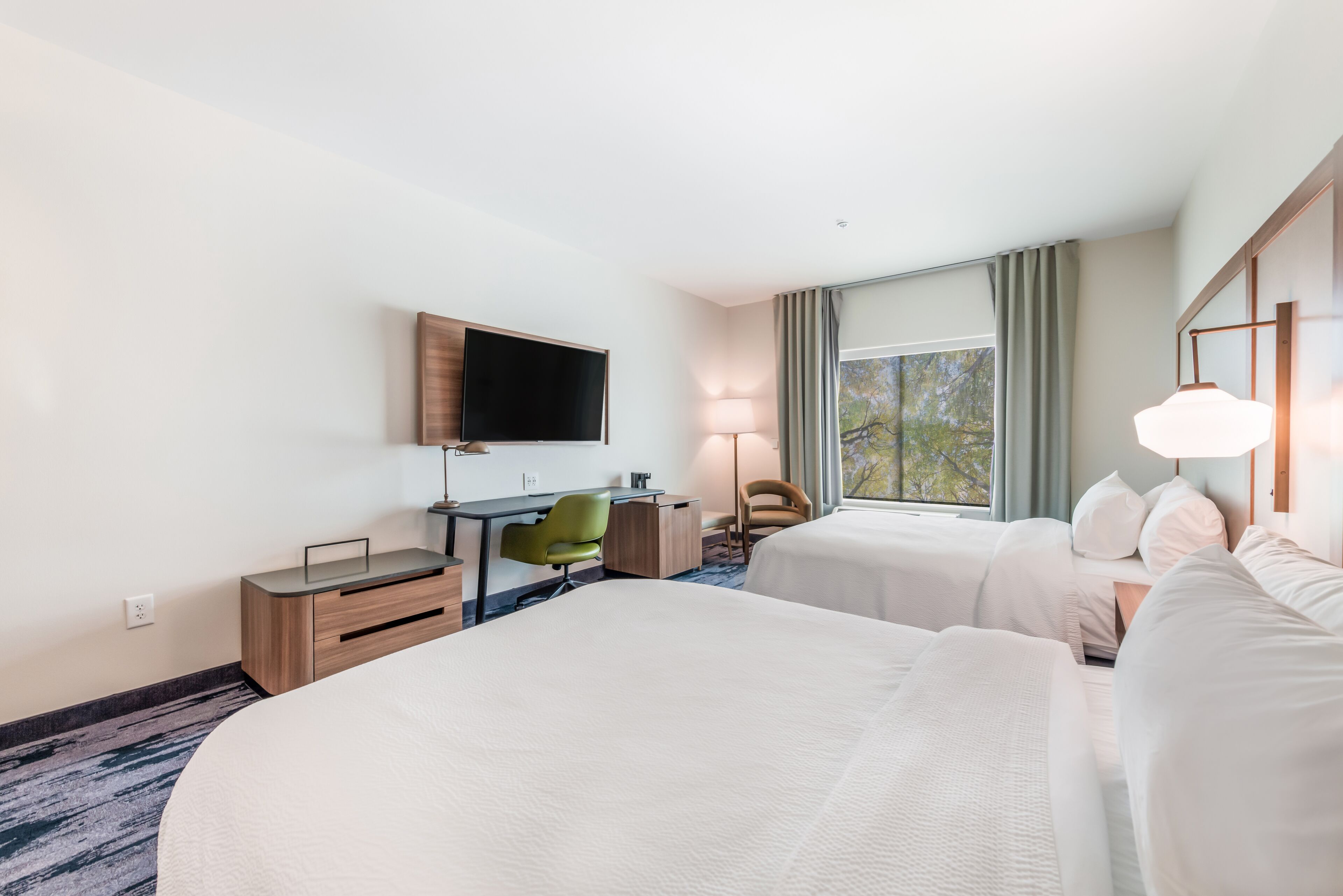 A hotel room with two beds, a desk, a chair, a TV, and a window with curtains.