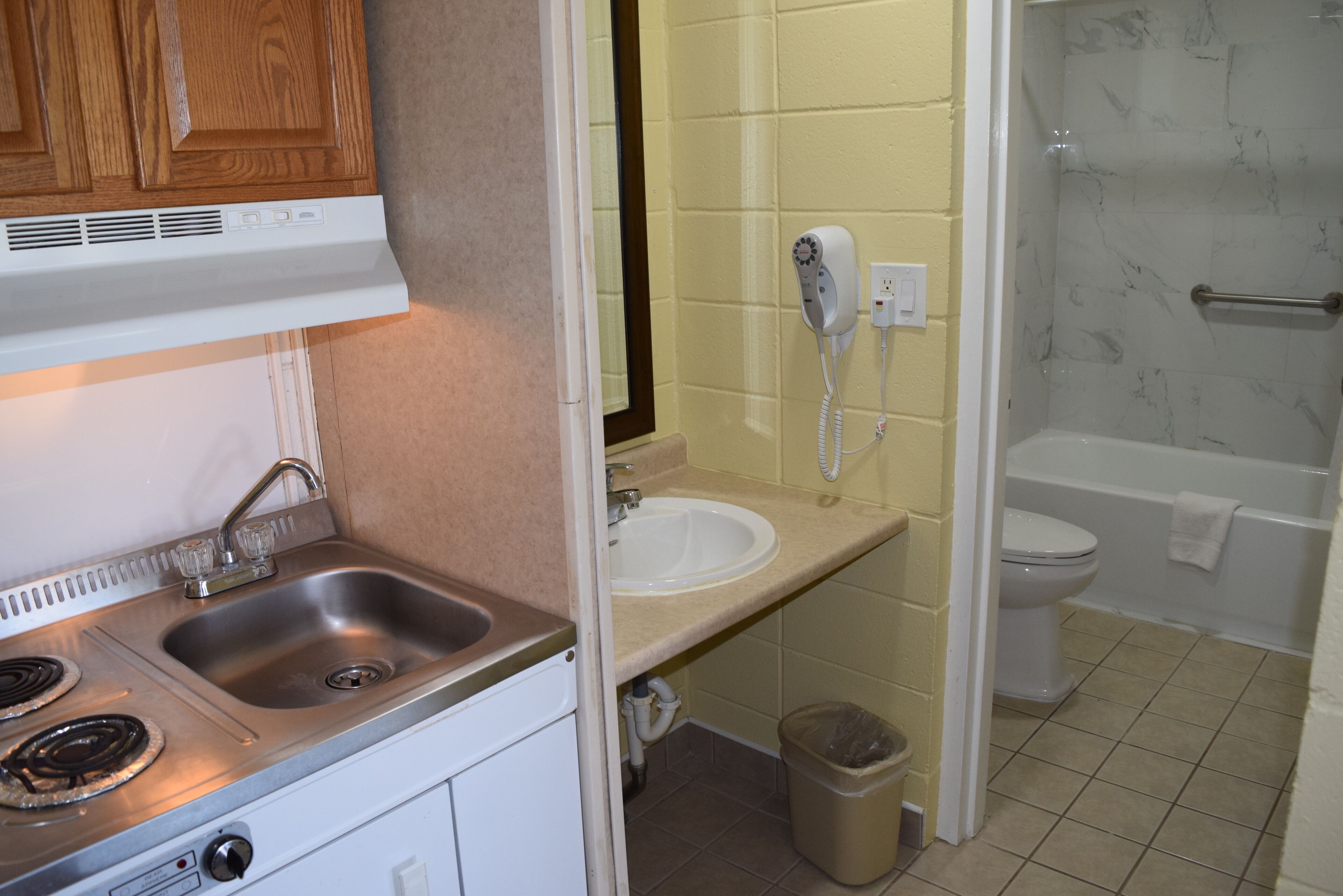 Een keuken met een spoelbak, fornuis en kastjes; een badkamer met toilet, bad en douche; en een haardroger aan de muur.
