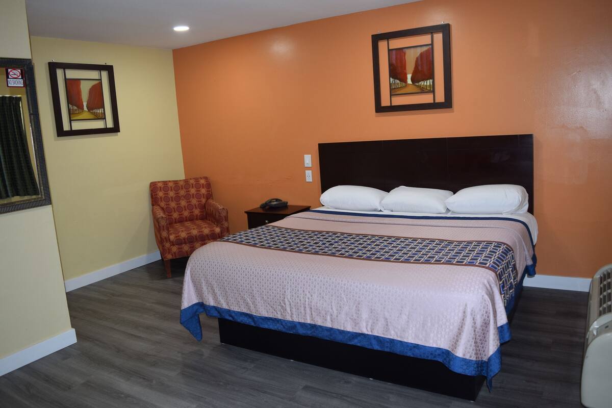 A hotel room with a large bed, a chair, a nightstand, and two framed pictures on the wall.
