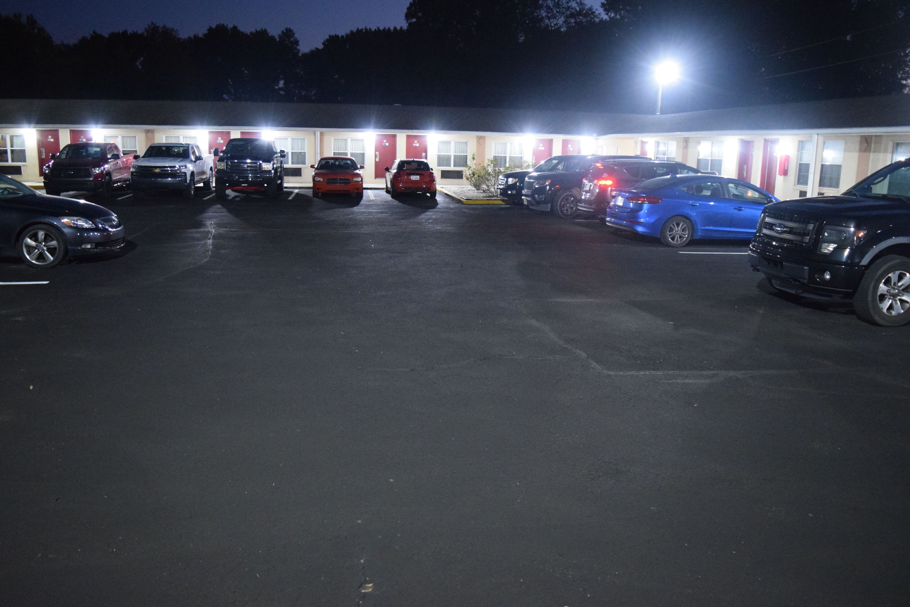 Ein Parkplatz mit mehreren parkenden Autos vor einem Gebäude mit roten Türen und weißen Wänden.