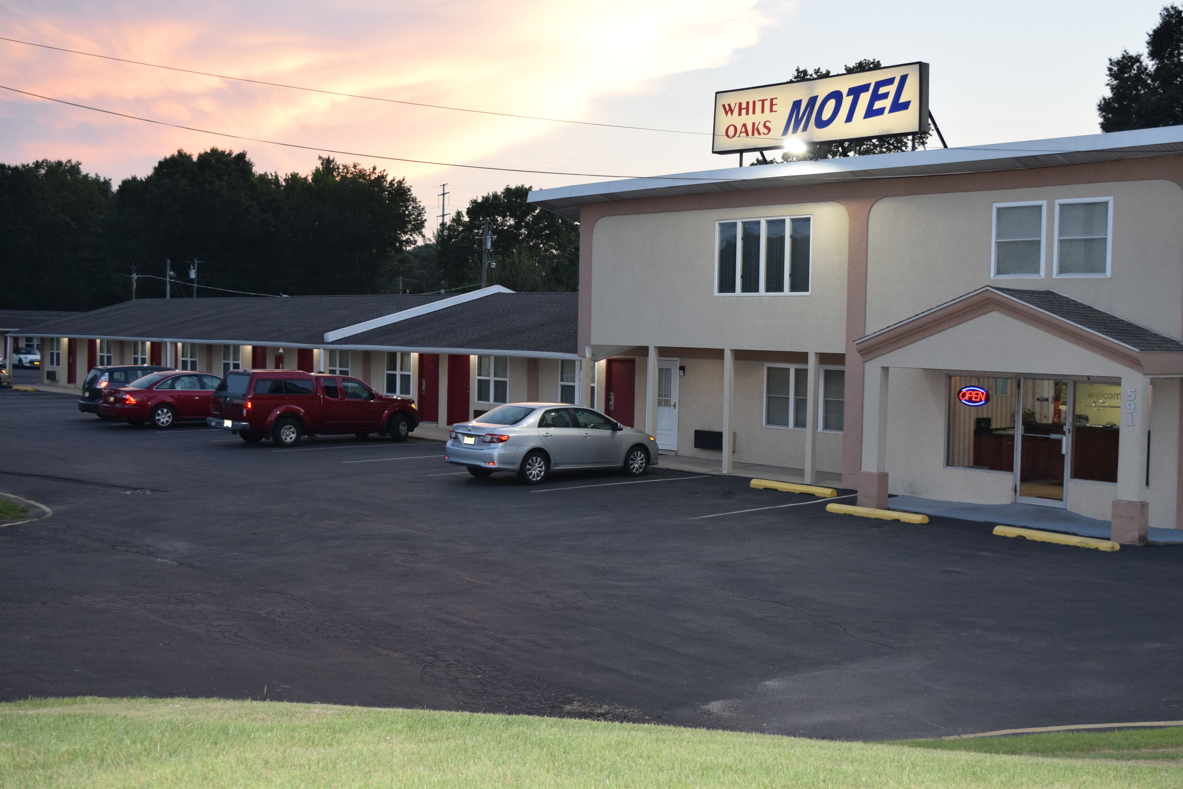 Un motel con un letrero que dice "White Oaks Motel". Varias coches están estacionados al frente, y el edificio tiene un diseño sencillo y funcional con techo plano.