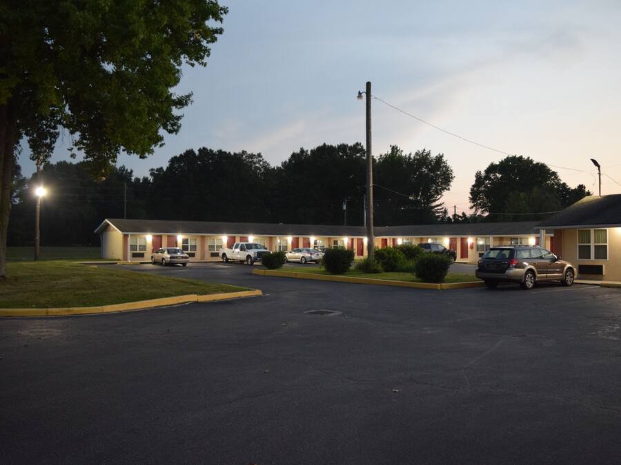 Un motel con varias habitaciones, un estacionamiento y un exterior bien iluminado.