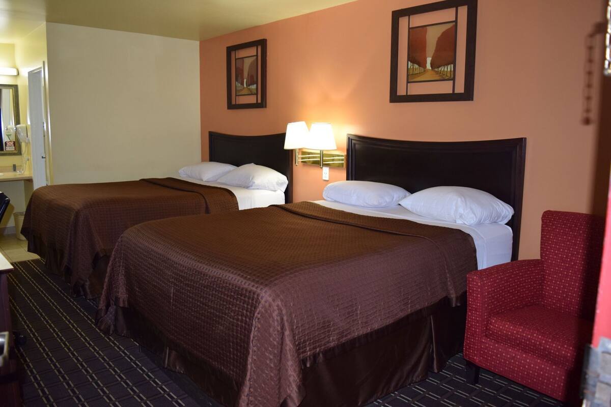A hotel room with two beds, a red chair, and a lamp.