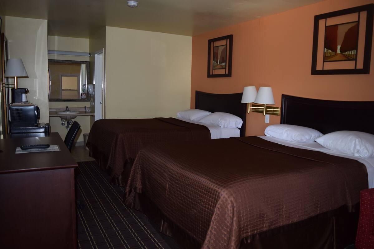 A hotel room with two beds, a desk, a chair, a lamp, a mirror, and a painting on the wall.