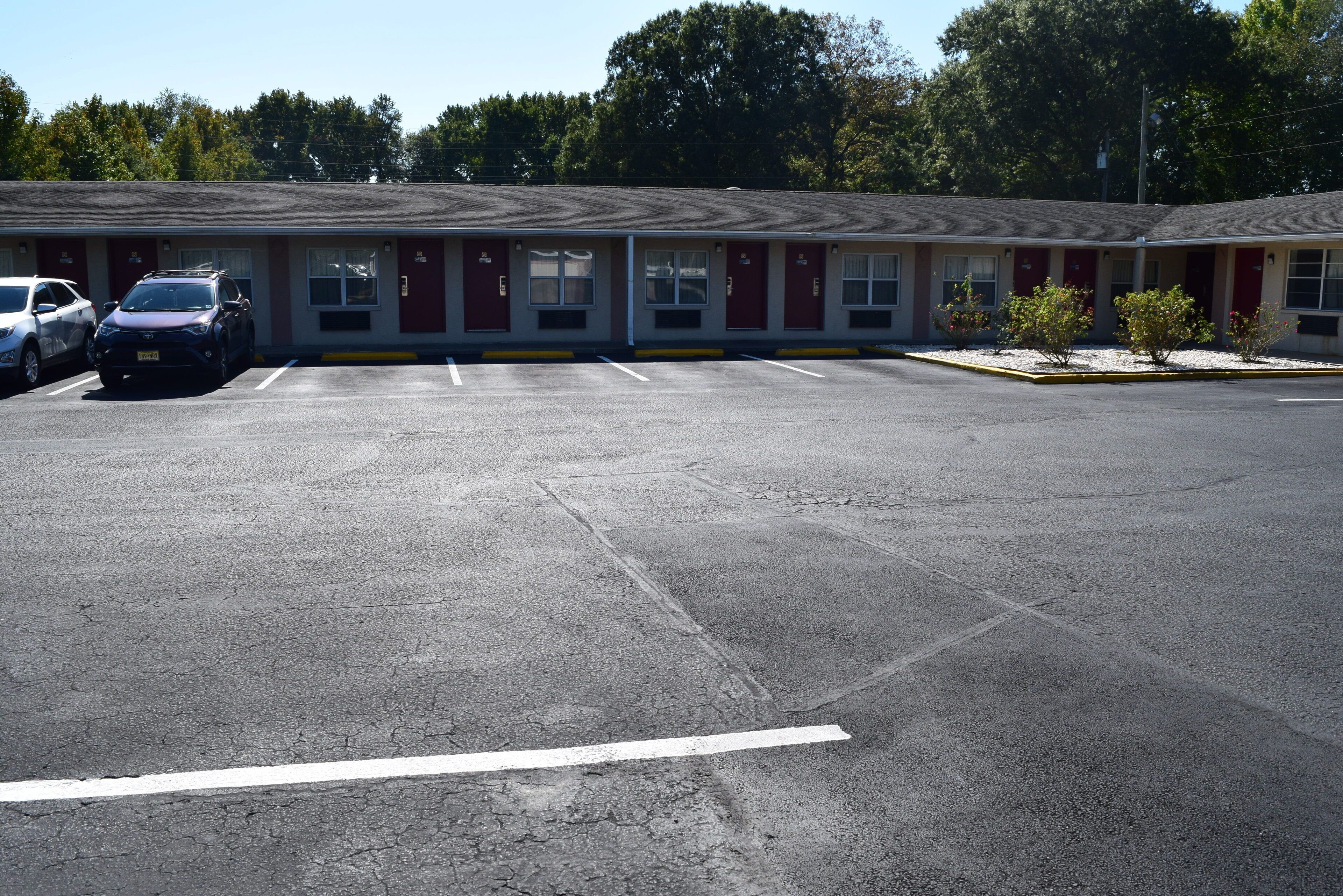 A motel with a parking lot, a building with red doors, and a few cars parked.
