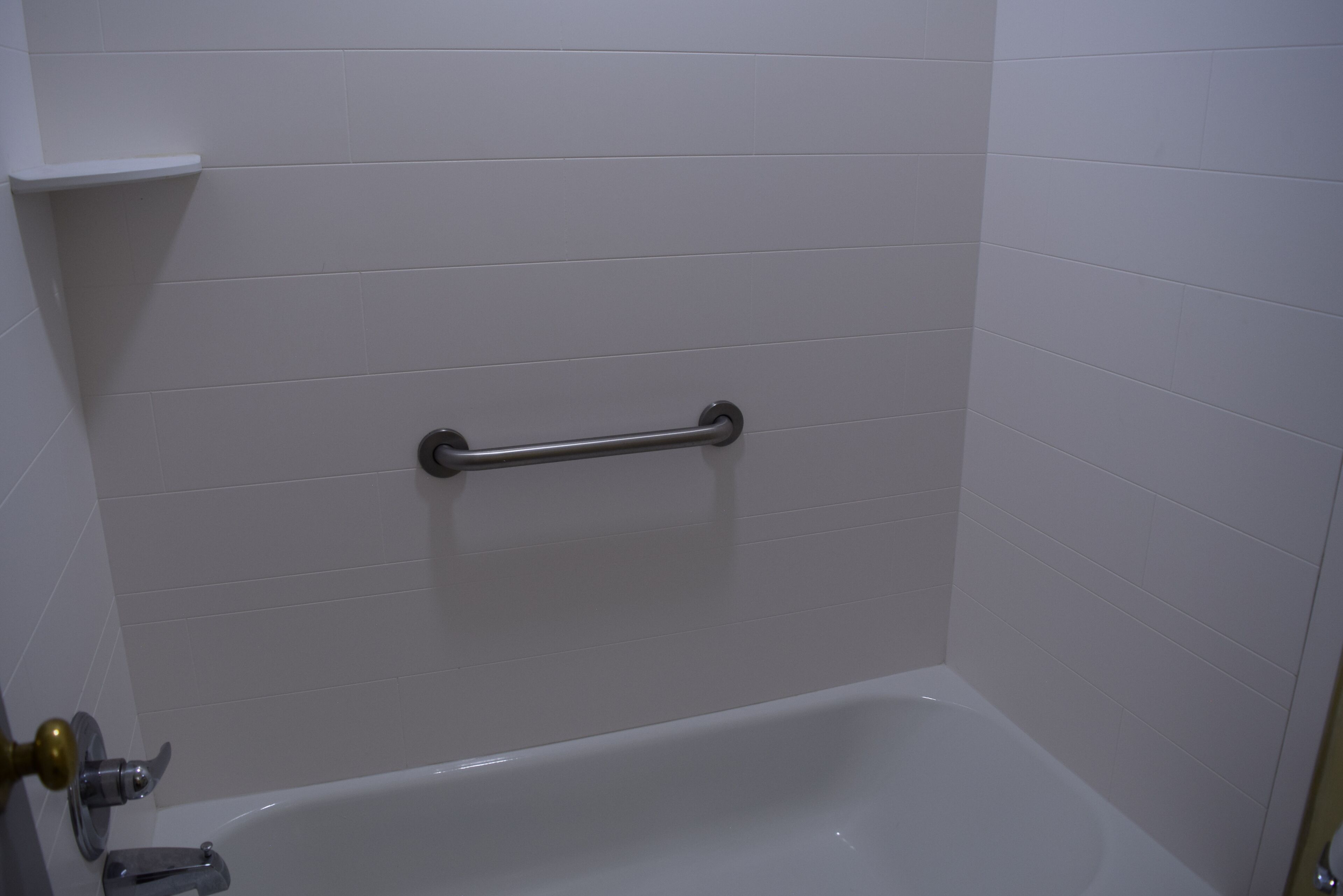 A bathroom with white tiled walls, a bathtub, and a grab bar.