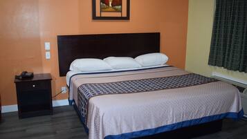 Hotelkamer met een groot bed, nachtkastje, schilderij aan de muur en een raam met gordijnen.