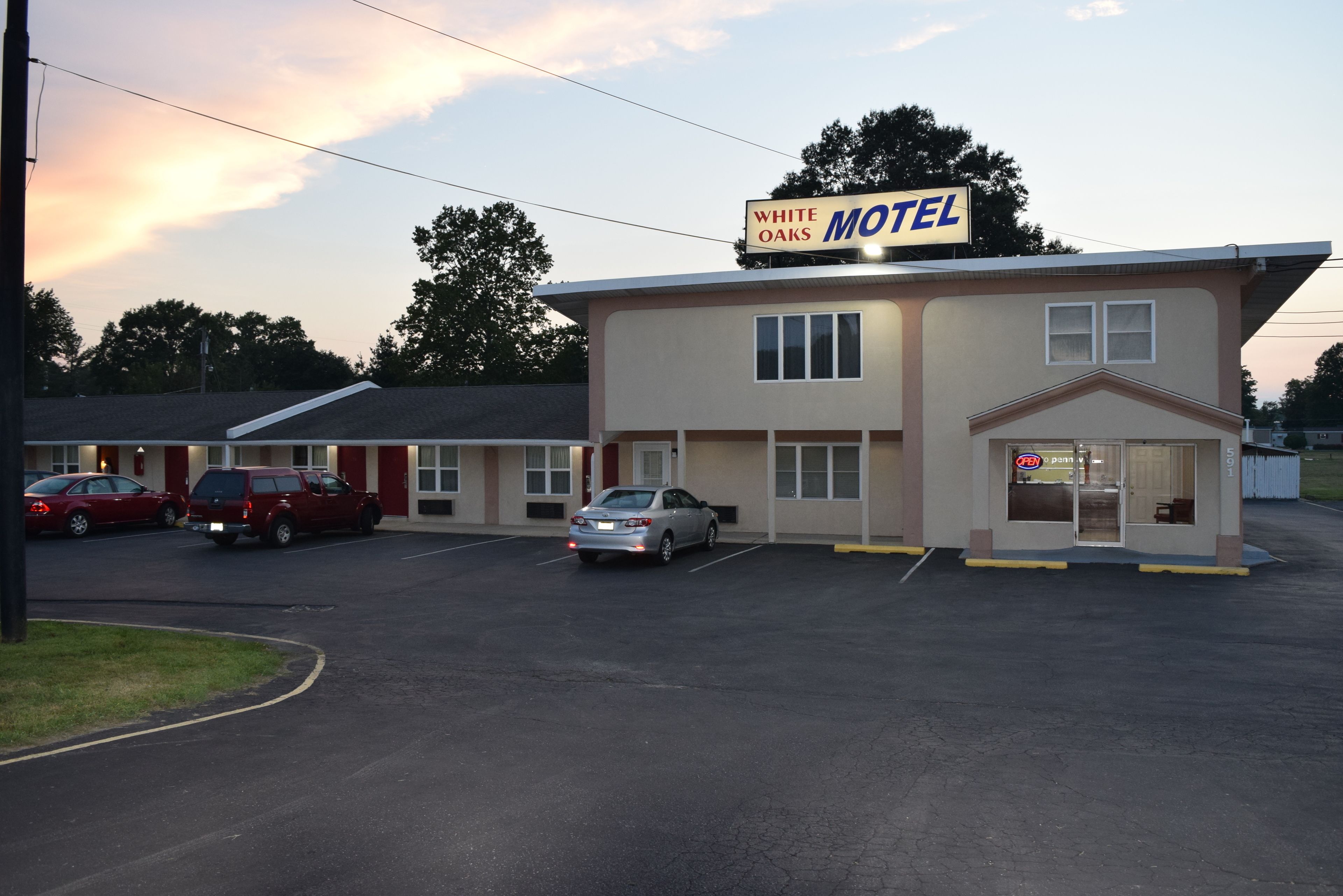 A motel with a sign reading "White Oaks Motel." There are multiple cars parked in front, and the building has a simple, functional design with a flat roof and a garage.