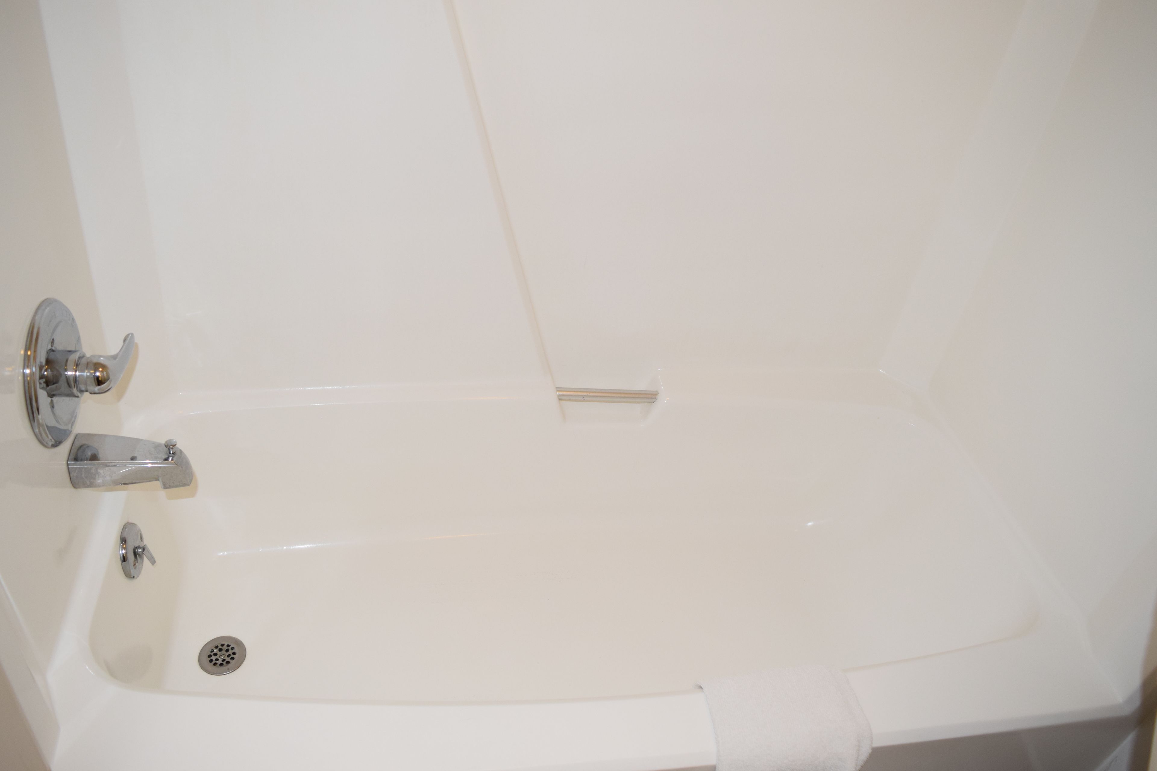 Una bañera blanca con desagüe, grifo y toallero.