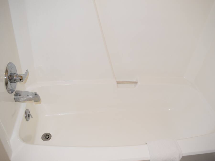 Una bañera blanca con desagüe, grifo y toallero.