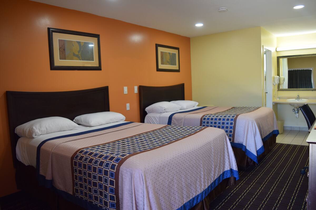 A hotel room with two beds, a bathroom with a sink, and two framed pictures on the wall.