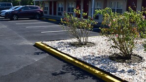 Un motel con aparcamiento, un pequeño jardín con plantas y un edificio con puerta roja.