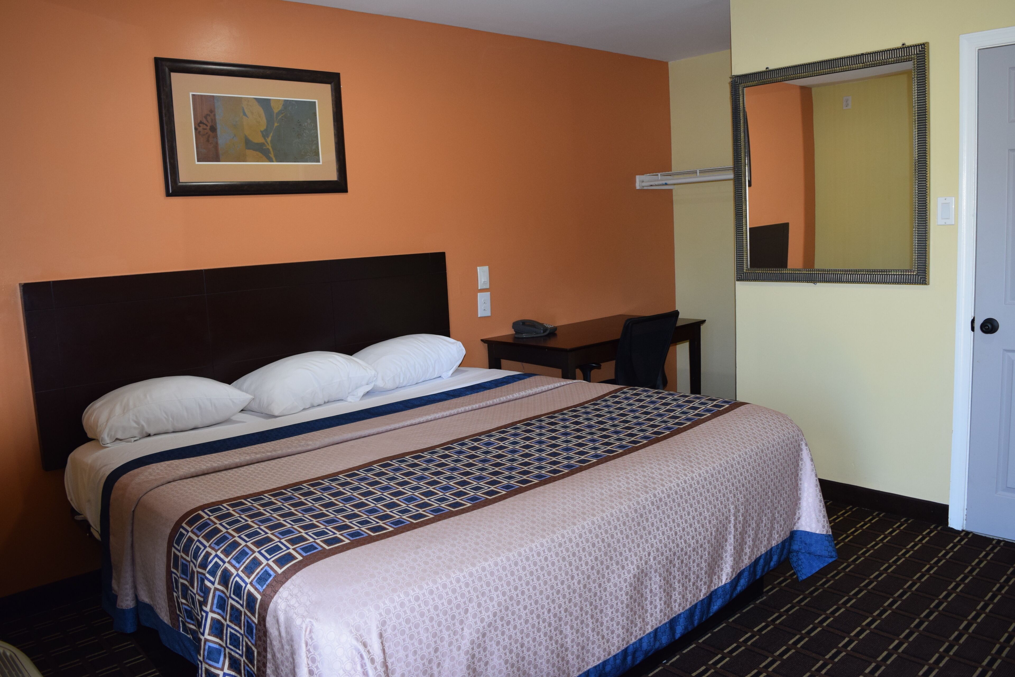 Una habitación de hotel con una cama grande, un escritorio, una silla, un cuadro en la pared y un espejo.