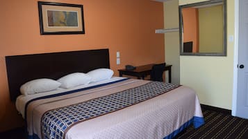 Una habitación de hotel con una cama grande, un escritorio, una silla, un cuadro en la pared y un espejo.