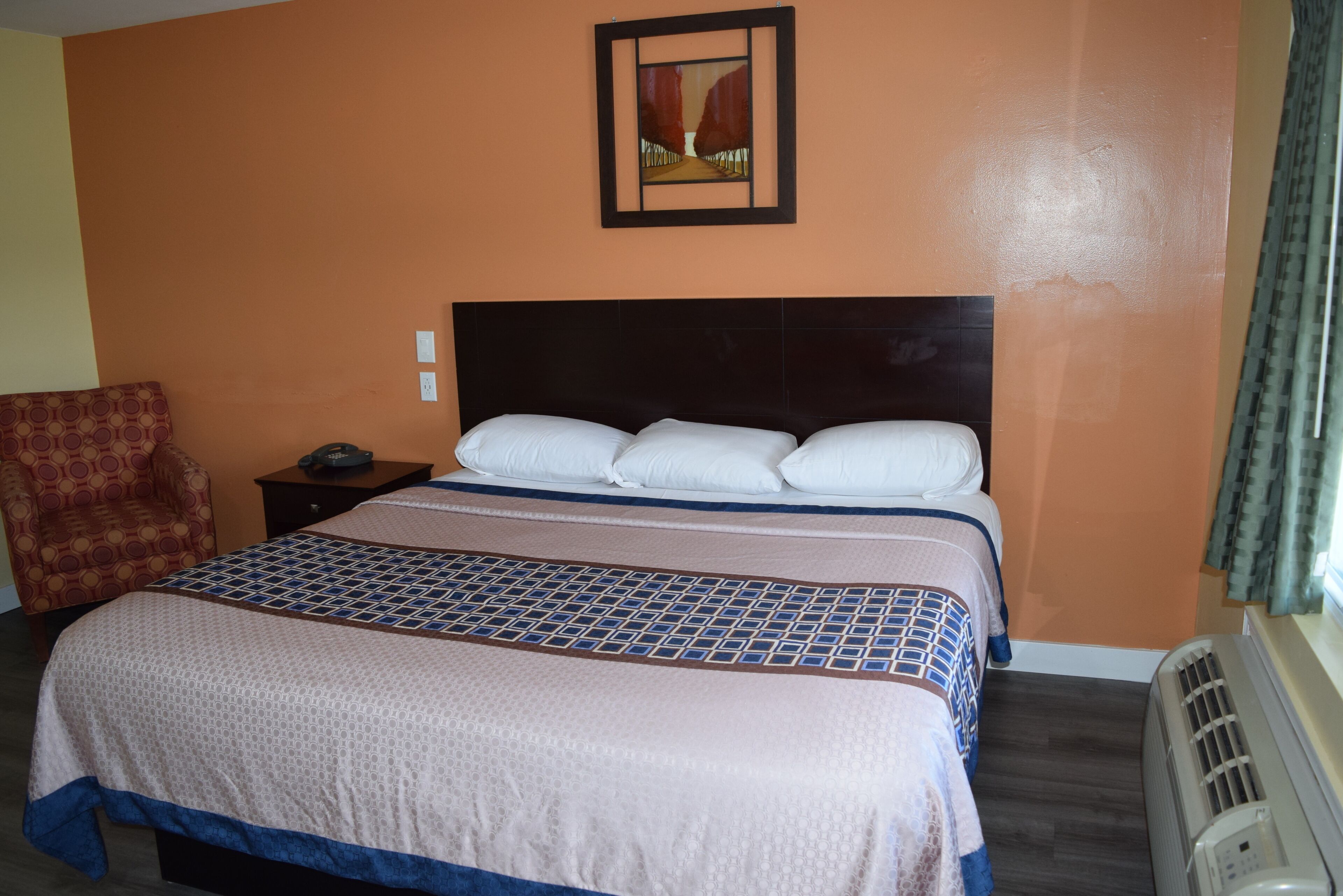 A hotel room with a large bed, a nightstand, a chair, and a wall-mounted picture.