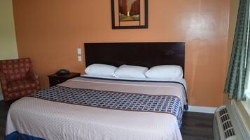 A hotel room with a large bed, a nightstand, a chair, and a wall-mounted picture.